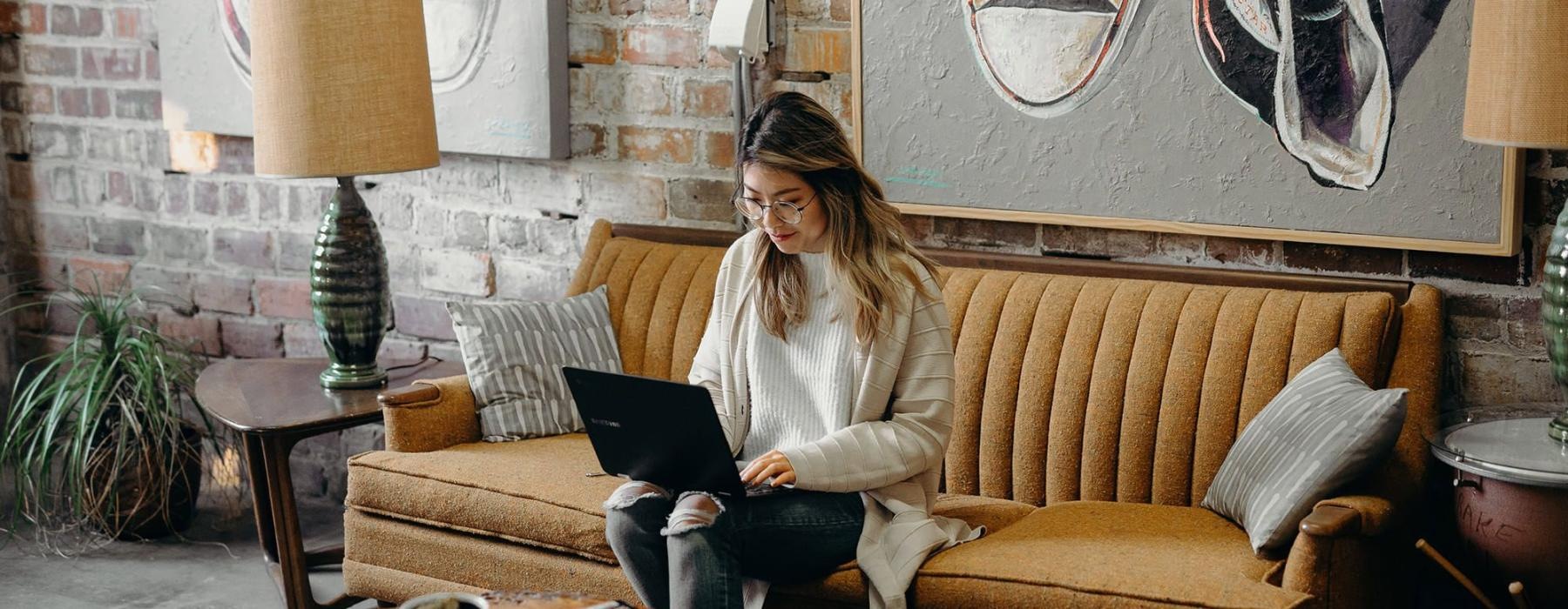 a woman sitting on a couch working on a laptop